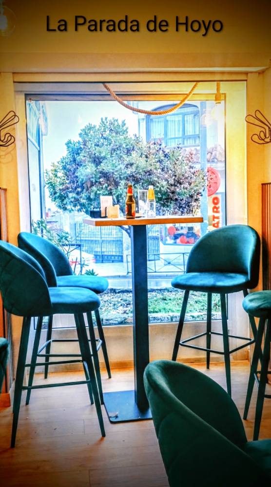 Mesas altas con taburetes de terciopelo verde junto a la ventana de La Parada de Hoyo